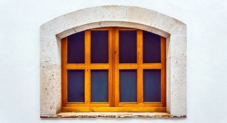 Fenêtre en arc en bois vieilli sur mur blanc de maison ancienne