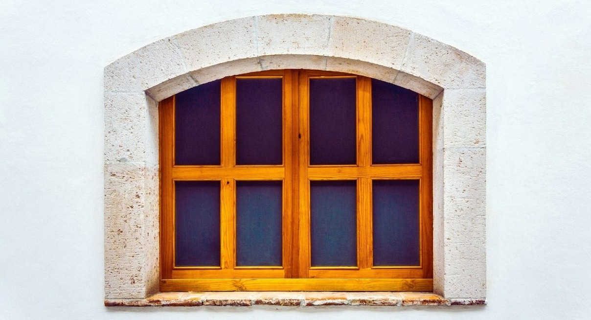 Fenêtre en arc en bois vieilli sur mur blanc de maison ancienne